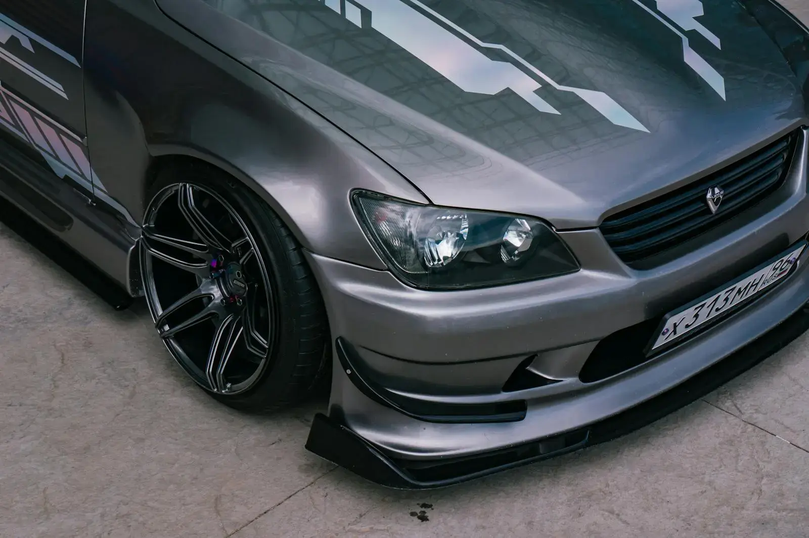 Close-up of a metallic sports car featuring custom graphics, low profile tires, and a stylish body kit.